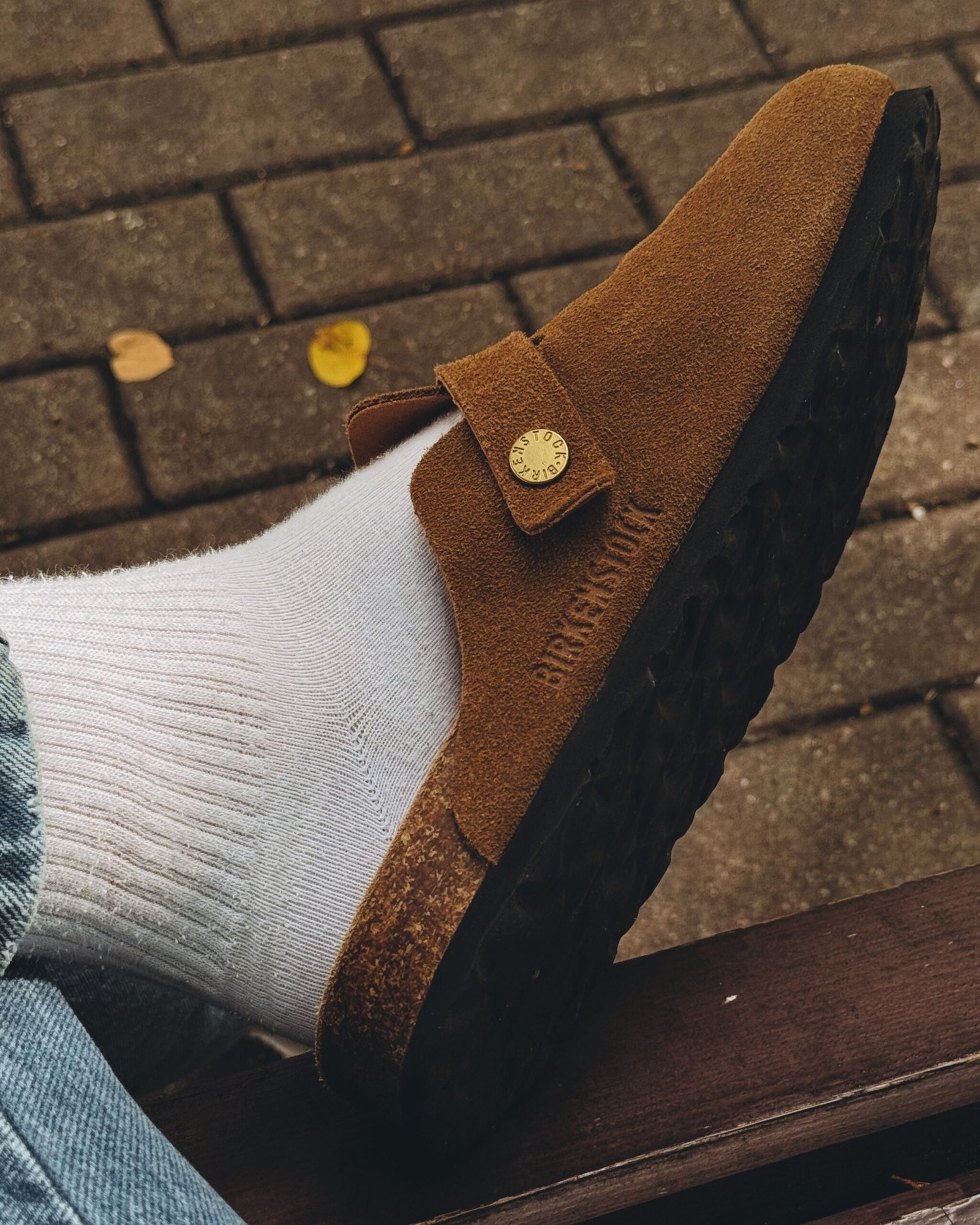 Close-up of a brown suede loafer and white sock on a cobblestone path, autumn vibe.