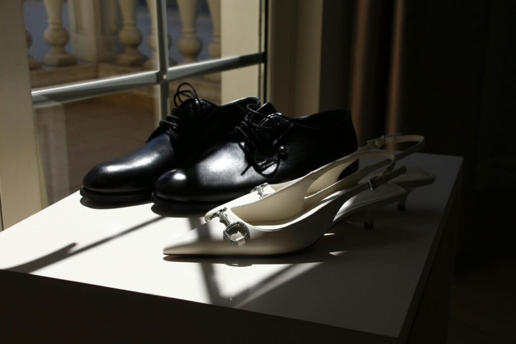 Close-up of stylish black men's and white women's shoes in sunlight by a window.
